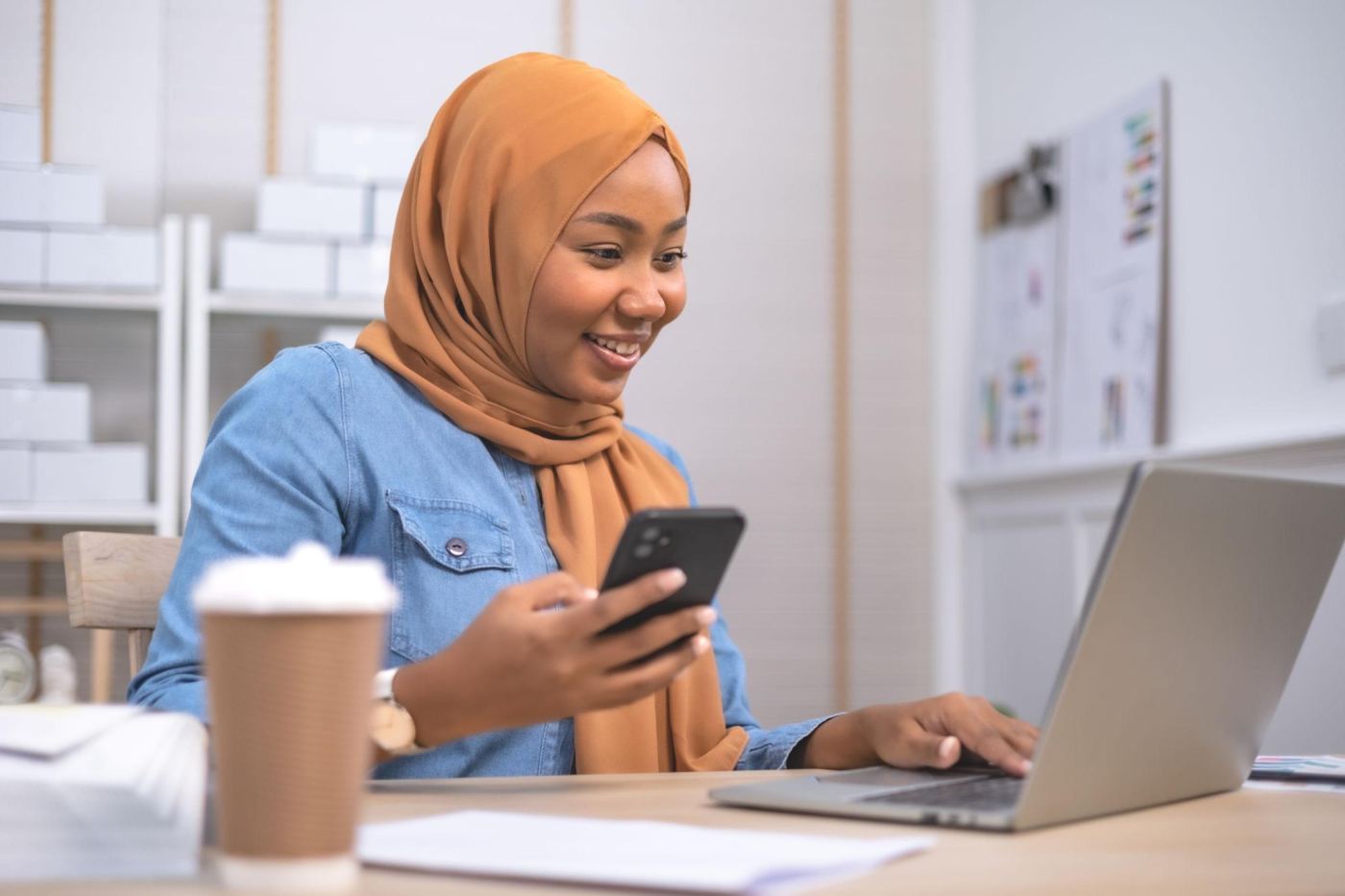 A woman checking her phone at her laptop